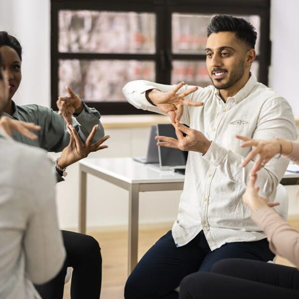 Grupo de pessoas se comunicando por meio da Língua Brasileira de Sinais em uma sala clara, representando inclusão e acessibilidade na comunicação. (Créditos: Depositphotos)