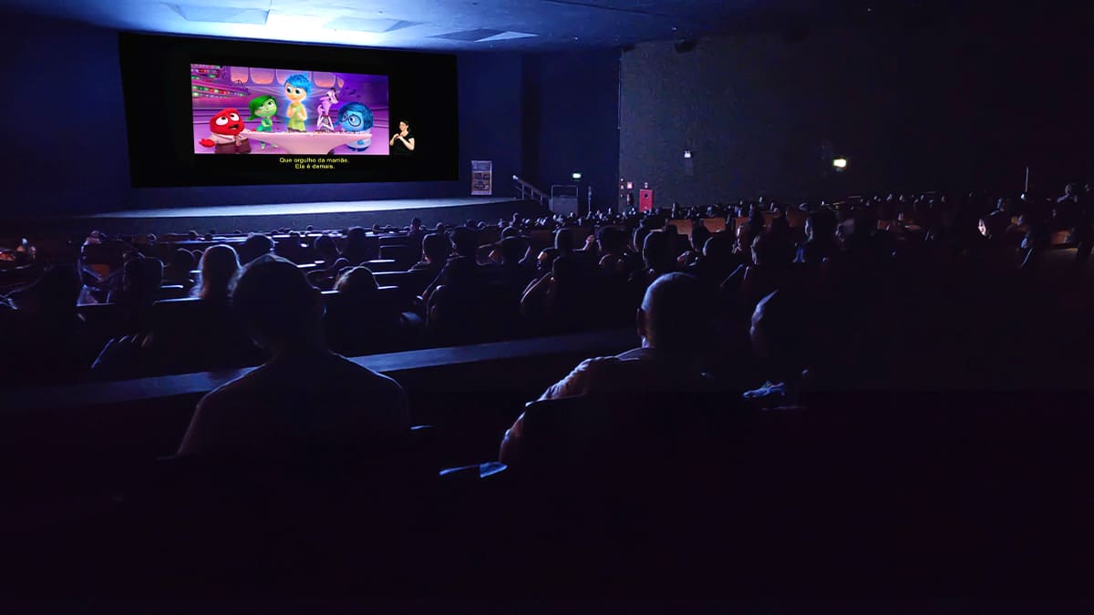 Público assiste ao filme “Divertida Mente” em cinema acessível com legenda em português e intérprete de Libras na tela. (Créditos: Divulgação)
