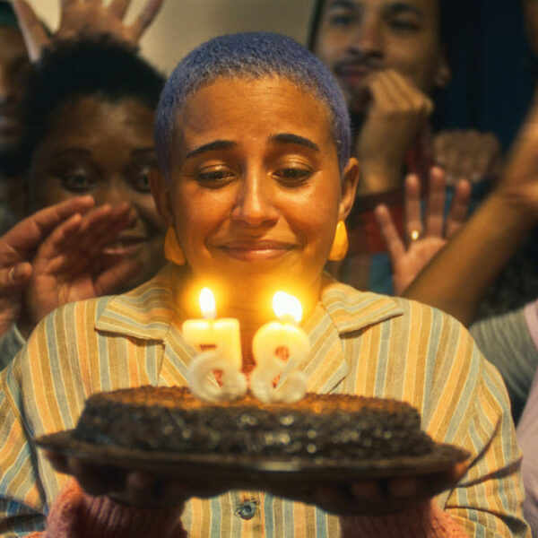 Pessoa segura bolo com velas de 35 anos, rodeada por amigos. Cena do filme "Nem Toda História de Amor Acaba em Morte", protagonizado pela atriz surda Gabriela Grigolom. (Créditos: Beija Flor Filmes)