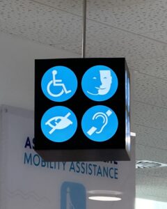 Exemplo de acessibilidade em bancos com placa suspensa com ícones azuis de cadeira de rodas, comunicação, deficiência visual e auditiva.
