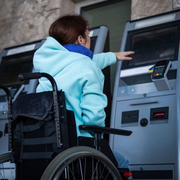 Pessoa em cadeira de rodas usando caixa eletrônico, destacando a importância de acessibilidade em serviços bancários. (Créditos: Depositphotos)