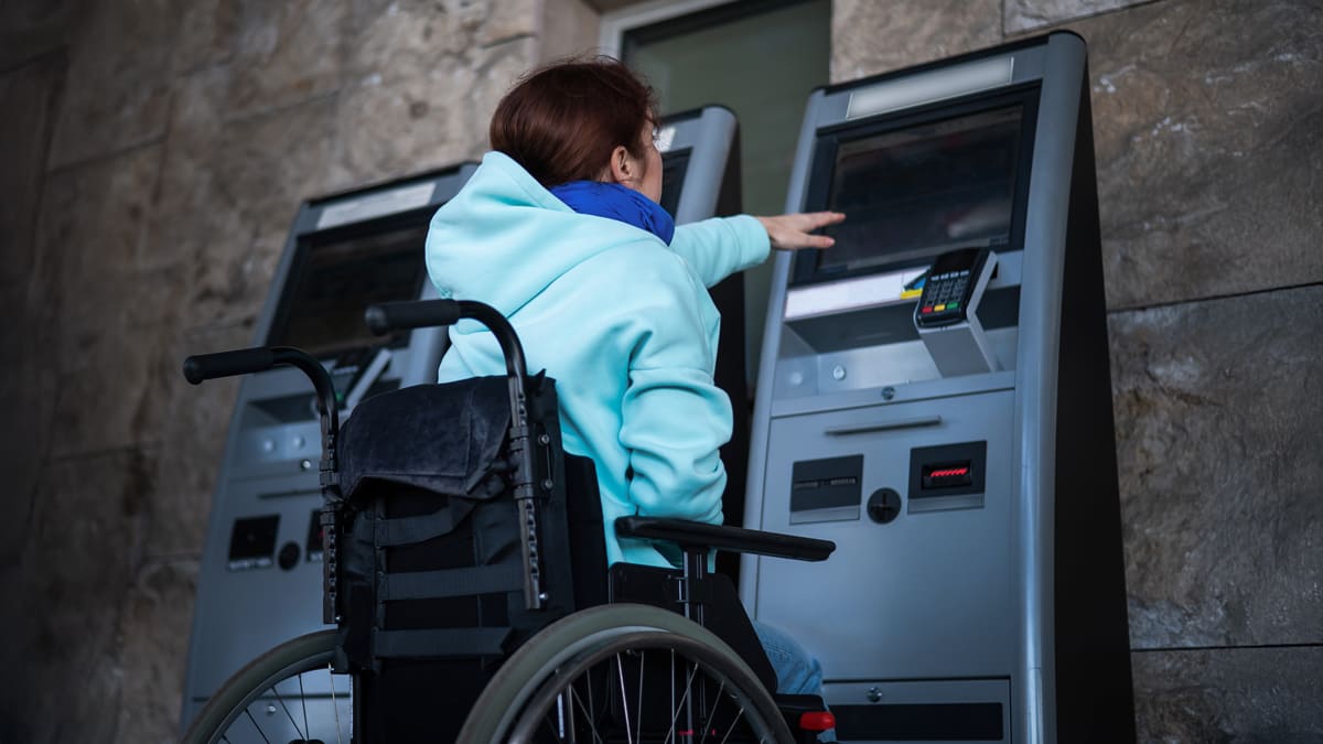 Pessoa em cadeira de rodas usando caixa eletrônico, destacando a importância de acessibilidade em serviços bancários. (Créditos: Depositphotos)
