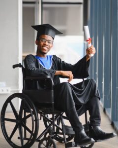 Estudante em cadeira de rodas sorri com beca de formatura e diploma na mão.