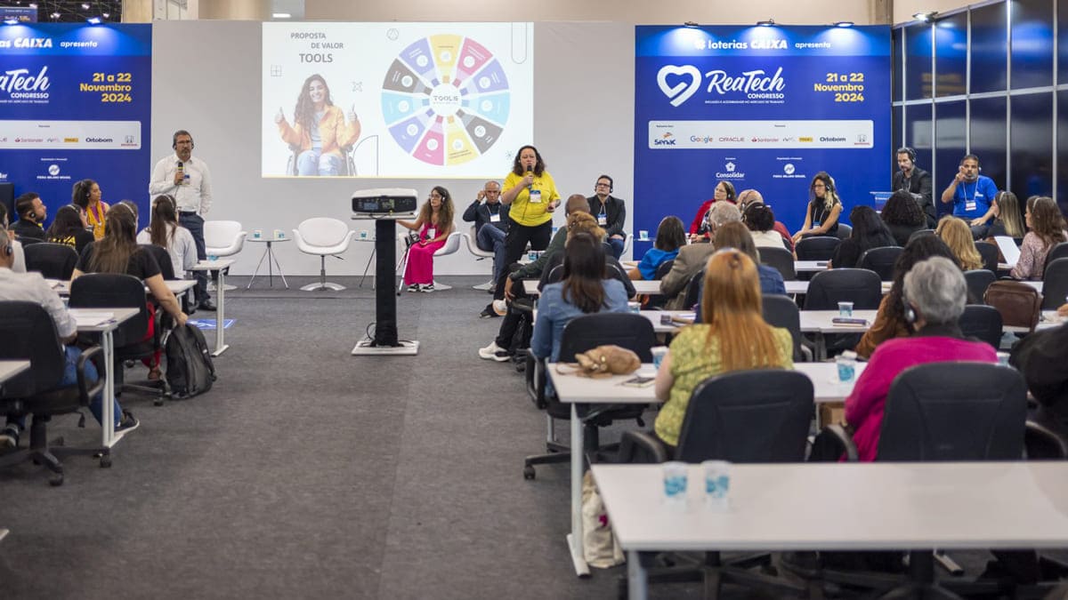 Palestra no Congresso Reatech com público, painel de especialistas e projeção em auditório. (Créditos: Reprodução / Reatech)