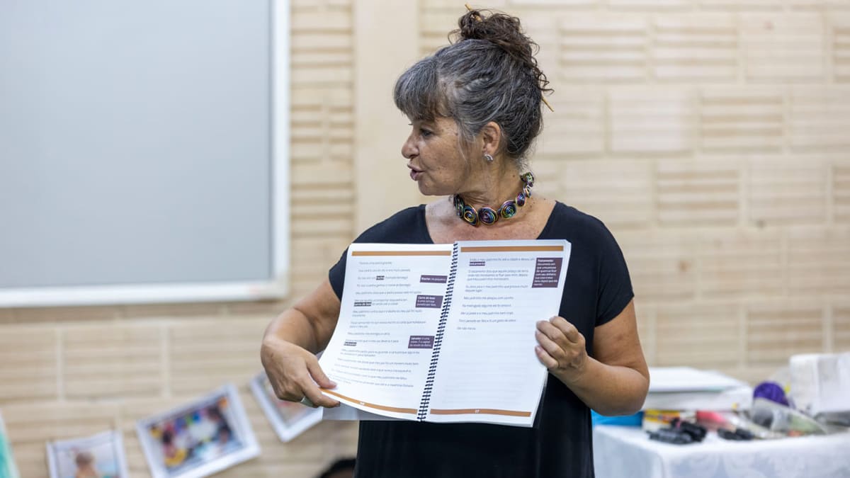 Carla Mauch, coordenadora da ONG Mais Diferenças, segura apostila aberta e explica conteúdo durante atividade formativa. (Créditos: Divulgação / Mais Diferenças)
