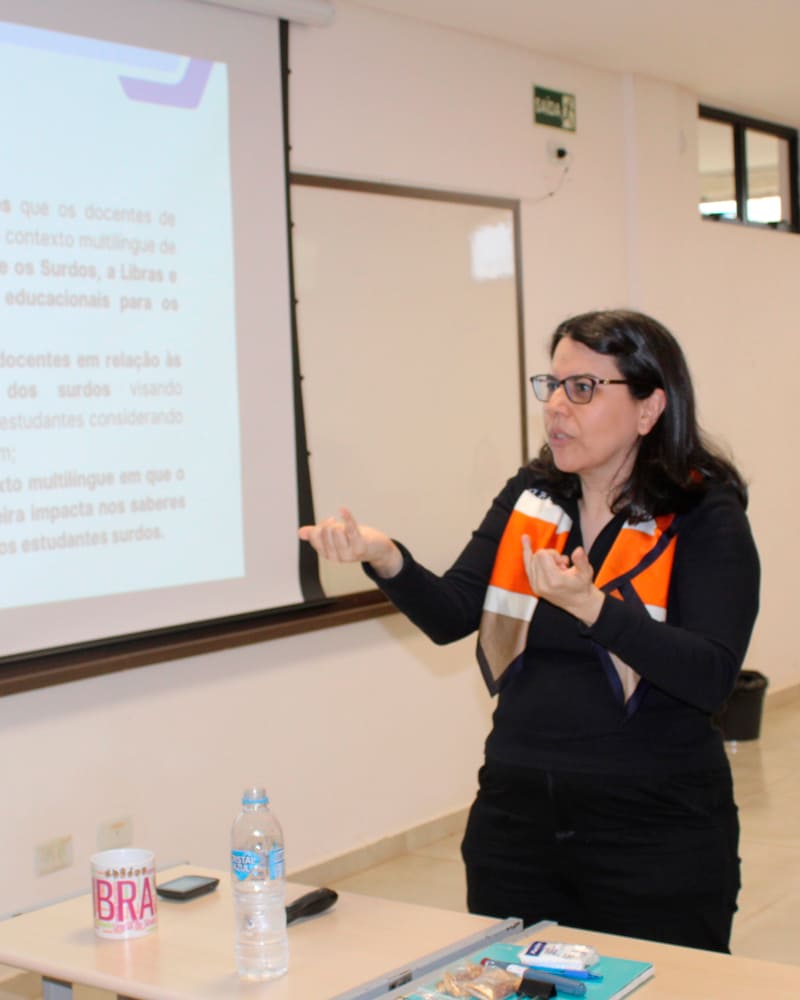 Primeira doutora surda da Unioeste, Andréa Mazacotte apresenta sua tese de doutorado em Libras, gesticulando em frente a um slide com seus objetivos.