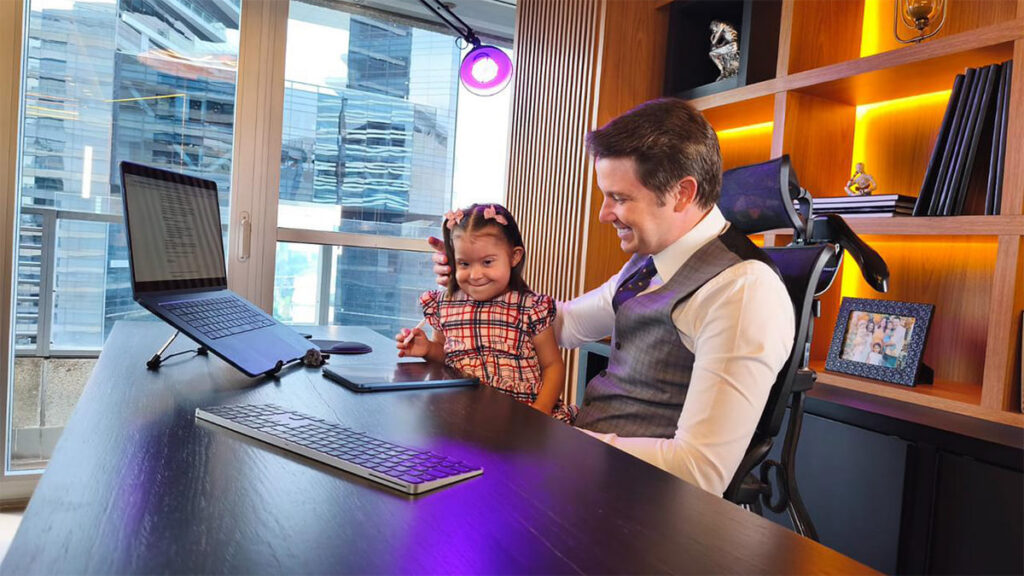 Márcio Zamboni, advogado, sorri para sua filha Maitê, com Síndrome de Down, em sua mesa no escritório.
