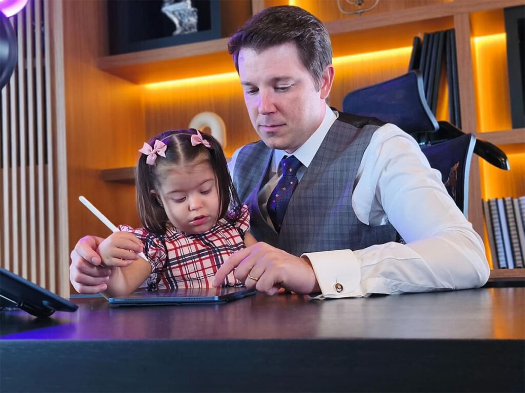 O advogado Márcio Zamboni observa sua filha Maitê, que tem Síndrome de Down, usando um tablet no escritório.