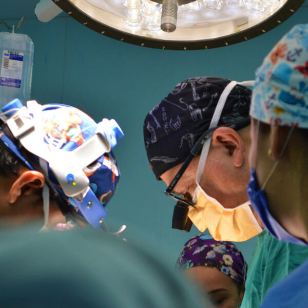 Equipe de cirurgiões usa lupas de precisão durante procedimento de implante neural, focados sob a luz do centro cirúrgico.