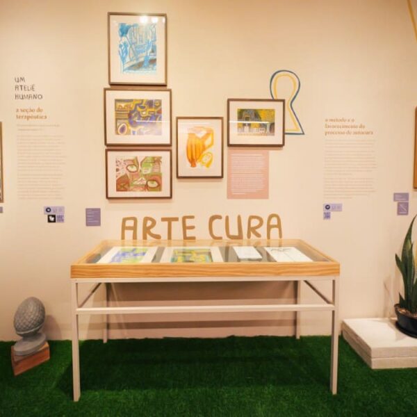 Fotografia da Exposição de Nise com seu retrato, quadros com gravuras e texto em destaque 'Arte Cura'.