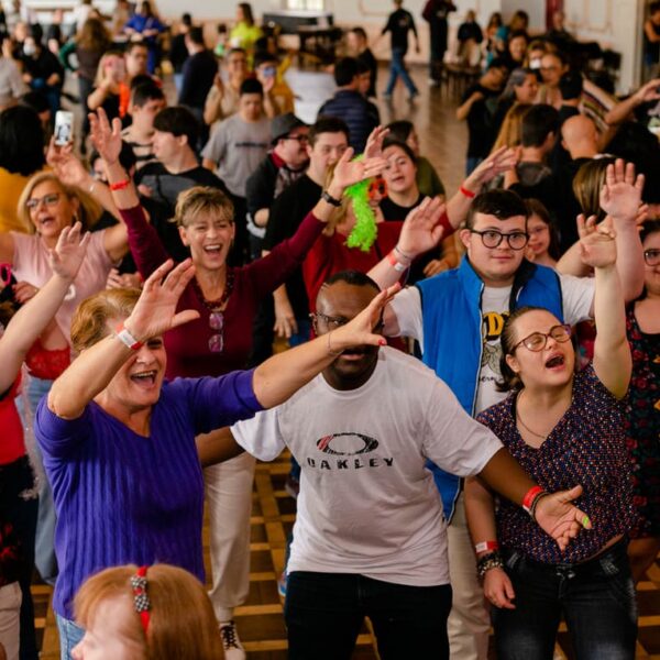 Carnaval Baladown: Grupo diverso de pessoas, incluindo jovens e adultos com Síndrome de Down, dançando com os braços levantados em um salão de festa.